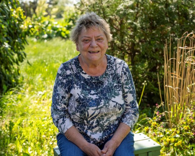 Kirsten Sørensen siddende på en bænk i sin skønne, vilde have. Foto: Dyrenes Beskyttelse