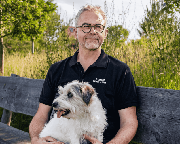 Jens Jokumsen sidder på en bænk i græsset med sin hund i skødet
