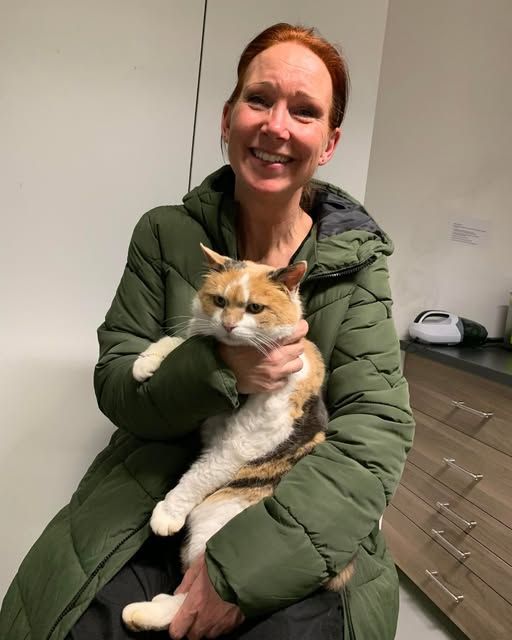 kvinde med rødt hår og grøn dunjakke sidder med kat på skød